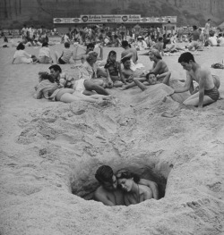  Young couple cuddling as they sit down in a hole in the sand