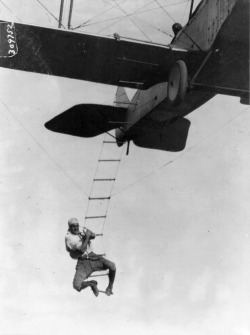 Fearless Freddie, a Hollywood stunt man, clinging to a rope ladder slung from a plane flown by A.M. Maltrup, about to drop into automobile below, 1921.