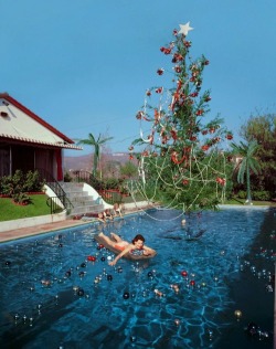 1950sunlimited:  A Christmas Swim, 1955 Photographer Slim Aarons took this picture of his wife Rita enjoying a swim amid a poolful of sparkling christmas ornaments.  when reading the description of this image it said Two children play in the background.
