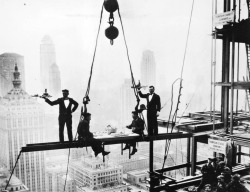 Two waiters serve two steel workers lunch, on a girder high above New York City, 14th November 1930.