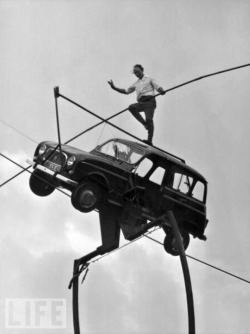 A high wire expert balances on the roof of a Renault car, which in turn is balanced on a rope.