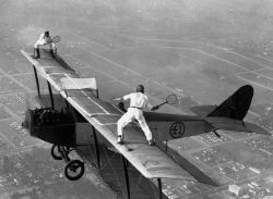 Professional airwalkers Gladys Roy and Ivan Unger playing tennis on the wing of a biplane in-flight, 1925.