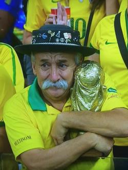 Old man with a mustache hugging a world cup while watching Brazil lose.