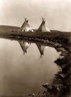 indypendenthistory:  Tepees at the Waters Edge. It was made in 1910 by Edward S. Curtis. The illustration documents Two tepees reflected in water of pond, with four Piegan Indians seated in front of one tepee.(via Tipis at Edge of Water) 