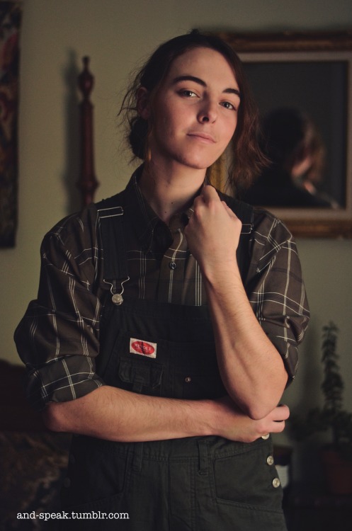 and-speak:  they/themrealized recently that overalls are very Gender ^_^[image description: three similar photos of op from the waist up. they wear dark green overalls over a dusty green plaid button down shirt. op is white with brown wavy hair worn up