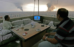 rad0:  People watching tv on balcony with black smoke rising in background Beirut Lebanon 