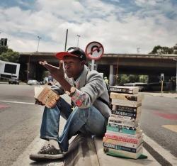 stunningpicture:  This young man sits on the side of Empire Road in South Africa and instead of begging he provides book reviews. He collects all these books, reads each of them, and provides reviews for people passing by. If you like the review, he will