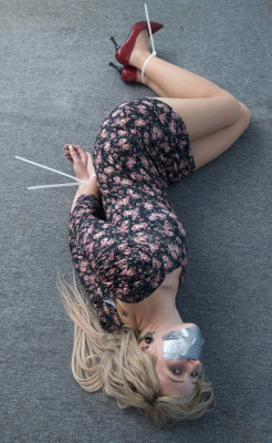 allthingsfetish:  Blonde babe lying on the floor tape gagged with her wrists and ankles zip tied wearing a tight short sexy dress