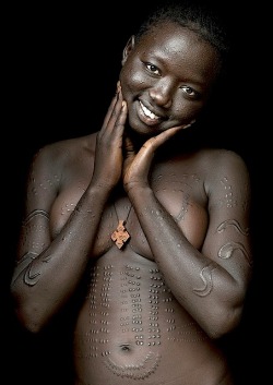 By   Eric LafforgueShe is called Anna, she lives in Hana Mursi village, in Omo valley, Ethiopia. She is from Bodi tribe. She had all those scarifications when she was 14. Since last year she has became christian, so she wears the cross around her neck