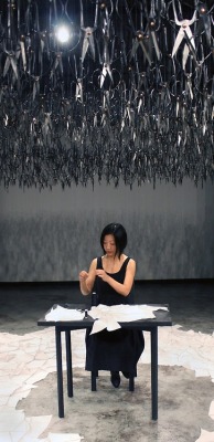  Beili Liu - The Mending Project (2011) “…Hundreds of Chinese scissors suspended from the ceiling in a shimmery cloud. The piece involved the artist sitting at a small black table, hand-mending patches of fabric together which visitors were encouraged