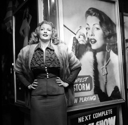 Tempest Storm poses next to one of the large lobby posters beneath the marquee at the ‘New Follies Theatre’; located in Los Angeles, California..
