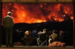 Grounded helicopter pilots watch as a forest fire rages on Mt. McLean, BC